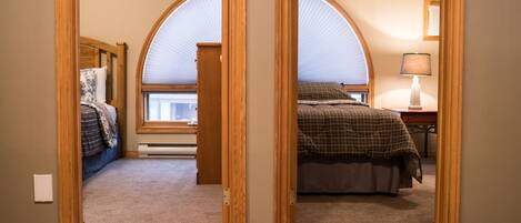 Une chambre à coucher avec une grande fenêtre en arc de cercle, un lit recouvert d’une couverture à carreaux et une table de chevet avec une lampe.