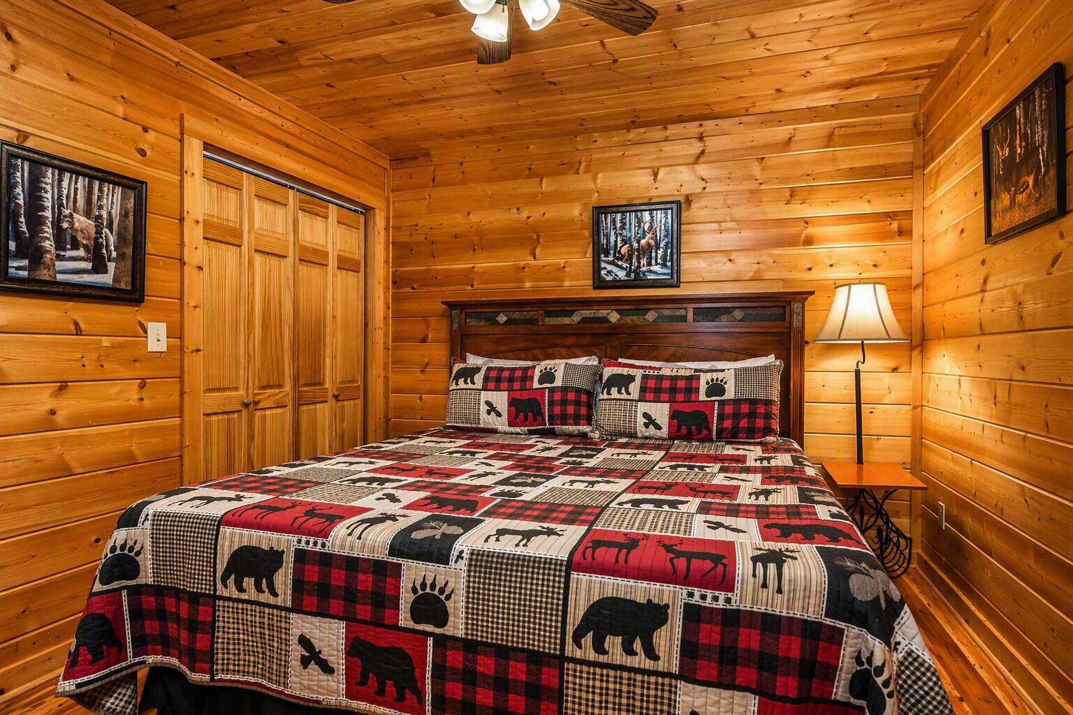 A wooden cabin bedroom with a bed, a nightstand, a lamp, and a framed picture on the wall.