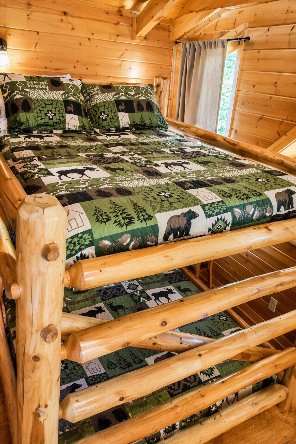 A wooden bed with a quilt featuring animal patterns, a window with curtains, and a wooden headboard.