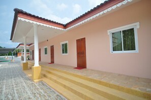 A building with a pink exterior, white columns, and a covered porch with steps leading to a door. - Tokyo Hotel (Lop Buri)