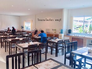 A restaurant with wooden tables and chairs, a large window with a view, and a wall with Thai text. - Tokyo Hotel (Lop Buri)
