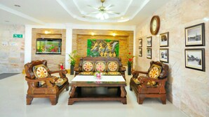 A lobby with a central coffee table, two wooden armchairs, a ceiling fan, a clock, and framed pictures on the walls. - Tokyo Hotel (Lop Buri)