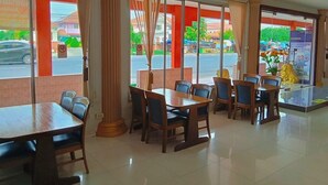 A restaurant with large windows, a tiled floor, and wooden tables and chairs. - Tokyo Hotel (Lop Buri)