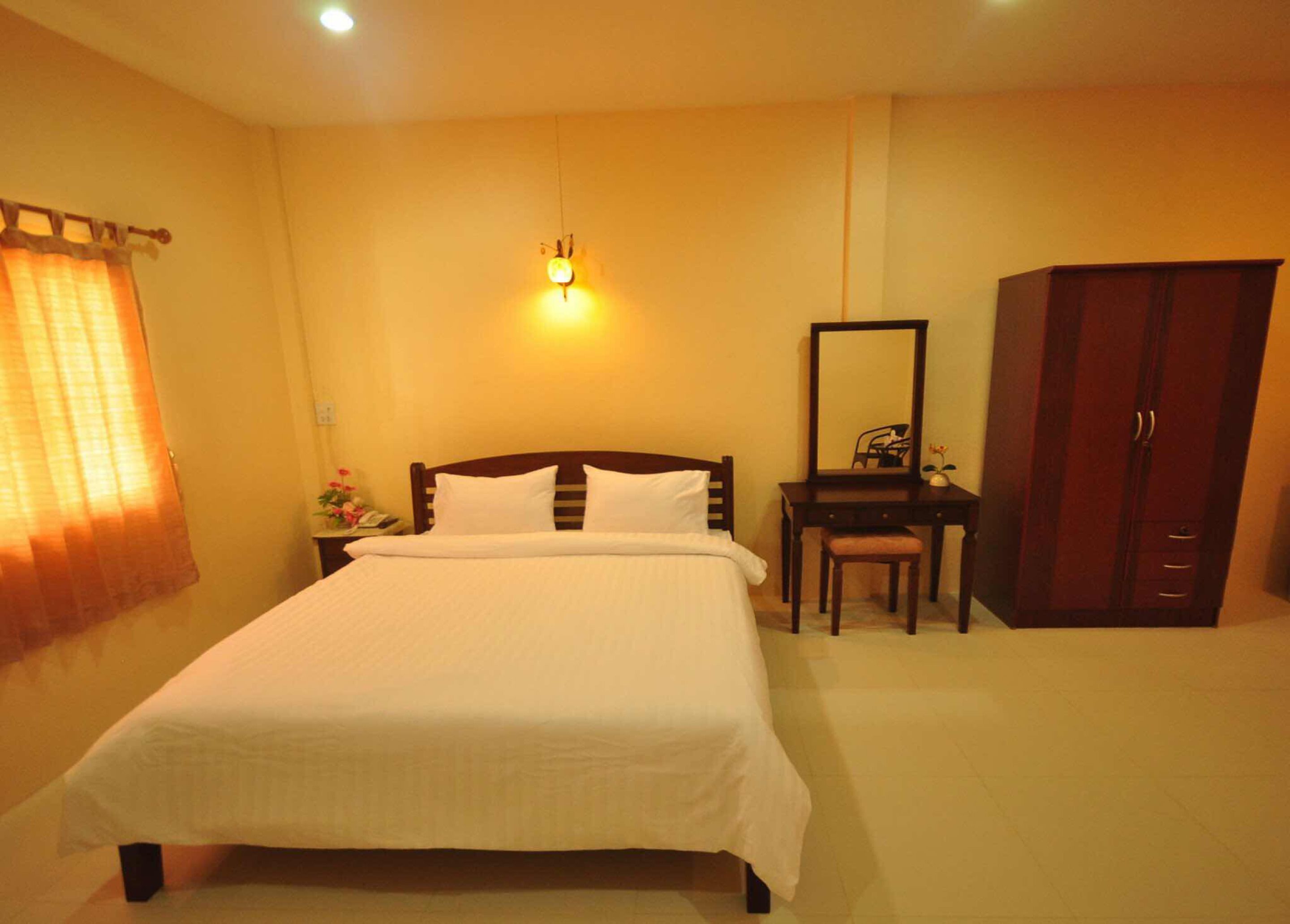 A hotel room with a bed, a desk, a chair, a wardrobe, and a nightstand with a lamp.