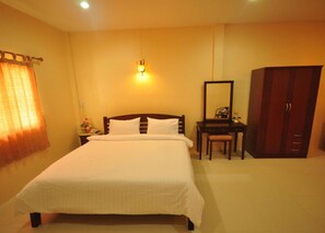 A hotel room with a bed, a desk, a chair, a wardrobe, and a nightstand with a lamp. - Tokyo Hotel (Lop Buri)