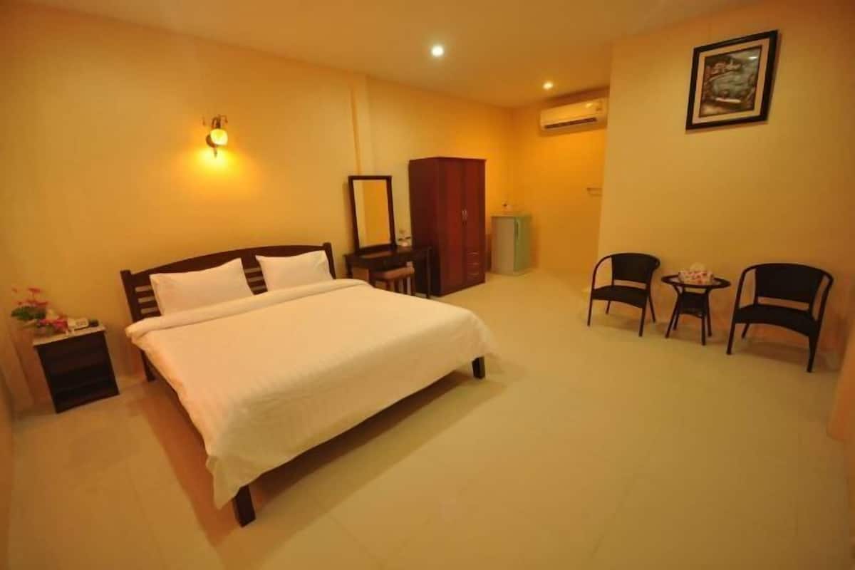 A bedroom with a bed, bedside table, dresser, mirror, two chairs, and a small table.