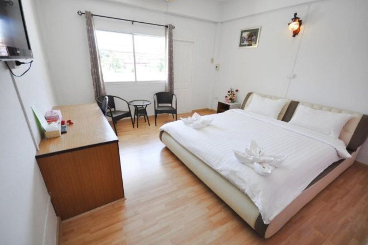 Una habitación de hotel con cama, escritorio, silla, mesita y ventana con cortinas.
