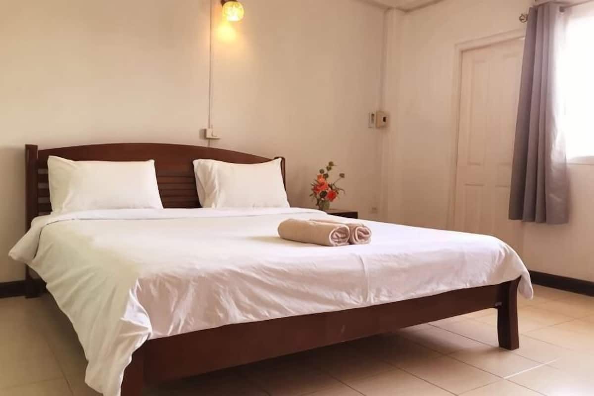 A neatly made bed with white linens, a wooden headboard, and a bedside table with a vase of flowers.