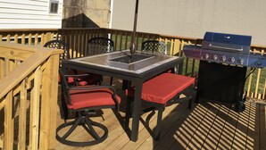 Eine Terrasse im Freien mit Tisch, Stühlen, einem roten Sonnenschirm und einem Grill.
