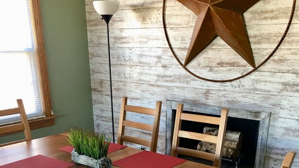 Ein Essbereich mit einem Holztisch, roten Platzsets und Stühlen. An der Wand ist eine Sternen-Dekoration und ein Kamin mit Holzscheiten.