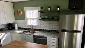 Eine Küche mit weißen Schränken, einem Edelstahlkühlschrank, einem Holztisch und einem Fenster mit Jalousien.
