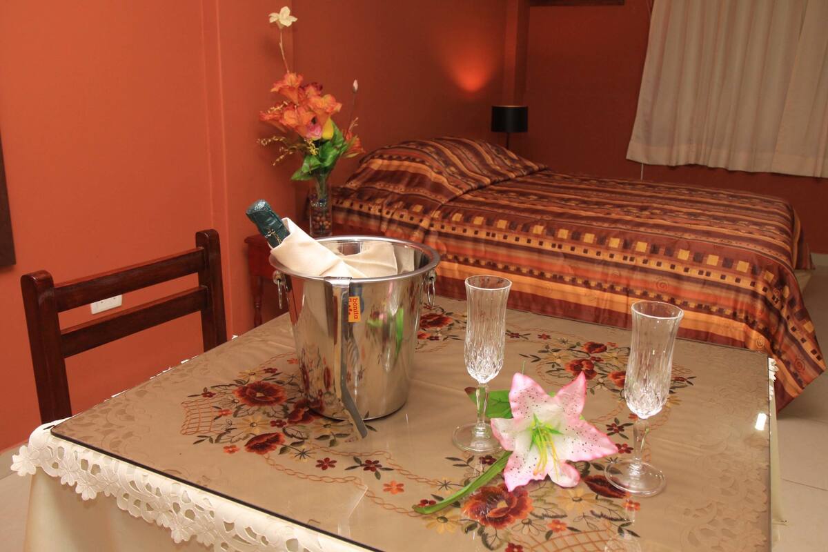 Ett hotellrum med ett matbord dukat för två personer, en metallhink, två vinglas och en blommig bordsduk.