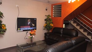 A living room with a leather sofa, a glass coffee table, a TV mounted on the wall, and a staircase with wooden steps. - Peru Hosting Piura (Piura)