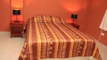 Una habitación de hotel con una cama grande, dos mesitas de noche con lámparas y un aire acondicionado instalado en la pared.