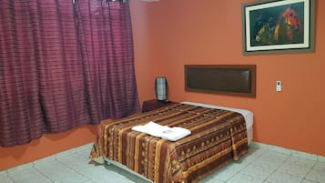 A room with a bed, a painting on the wall, and a curtain.