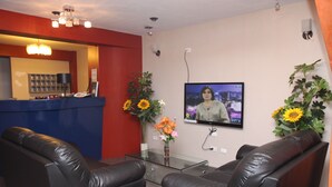 A reception area with a glass desk, two leather sofas, a TV on the wall, and sunflowers on either side. - Peru Hosting Piura (Piura)
