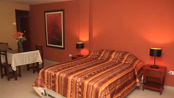 A bedroom with a large bed, two bedside tables with lamps, a small table with a vase of flowers, and a framed picture on the wall.