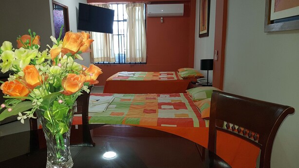 A hotel room with two beds, a TV, an air conditioner, a desk with a vase of flowers, and a chair. - Peru Hosting Piura (Piura)