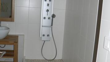 Una ducha con panel de control, un lavabo y un espejo.