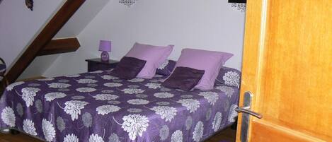 A bedroom with a bed, a nightstand, a lamp, and a wooden door.