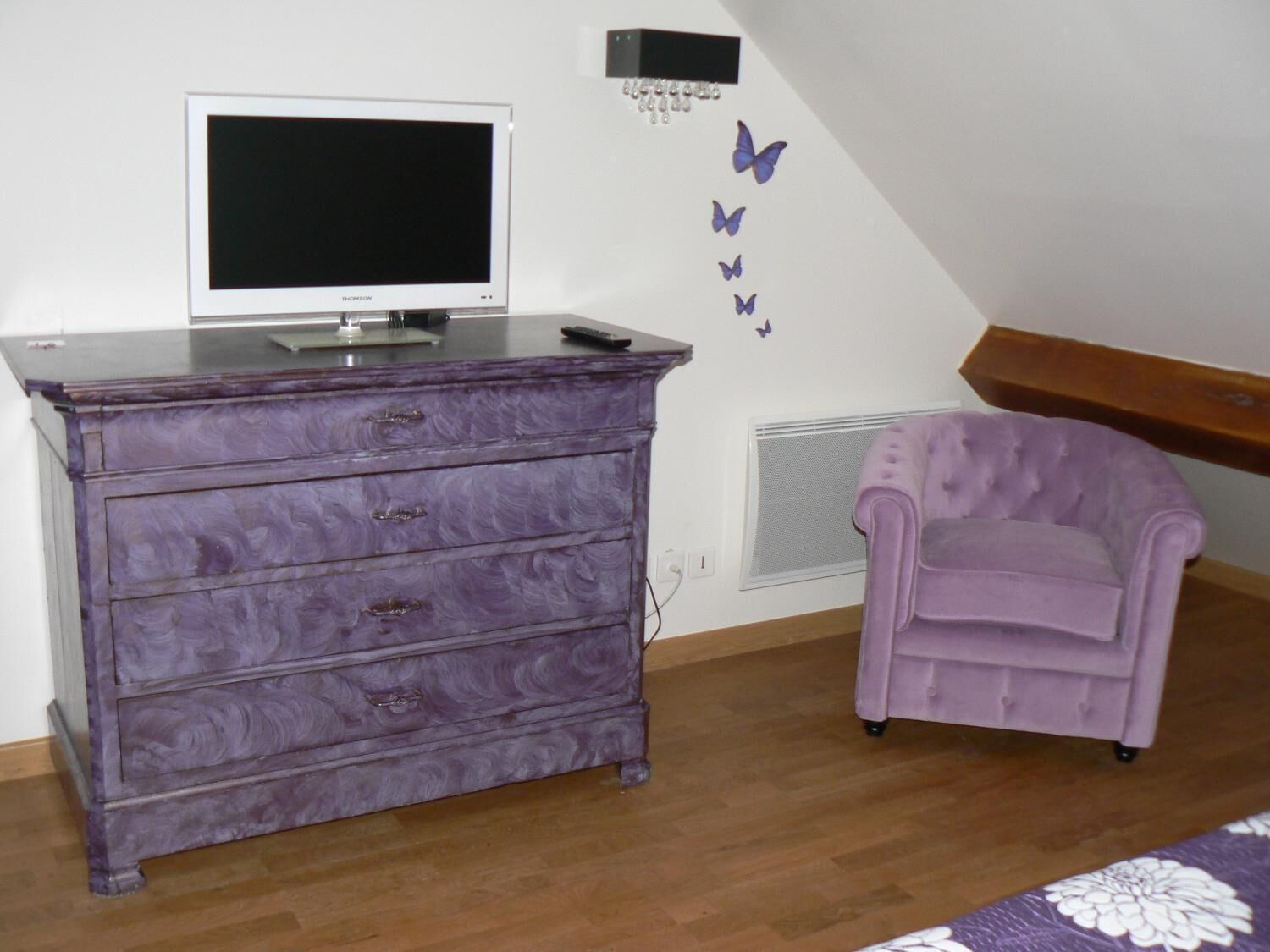 A room with a purple dresser, a television, a purple armchair, and a wall with butterfly decals.