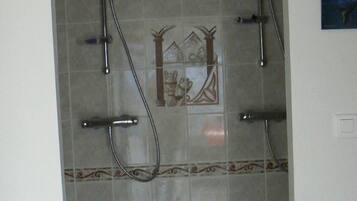 A shower area with a tiled wall, a decorative tile design, and a showerhead.