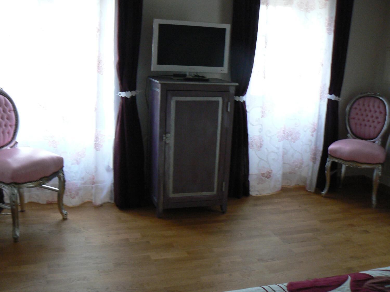 A room with a television on a cabinet, two chairs with cushioned seats, and a wooden floor.