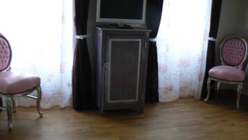 A room with a television on a cabinet, two chairs with cushioned seats, and a wooden floor.
