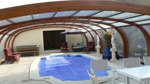 An indoor pool area with a covered roof, seating, and a table. - Le Manoir Des Chapelles (Venoy)