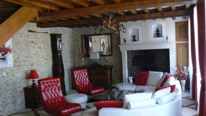 A living room with a white sofa, red chairs, a fireplace, and a stone wall. - Le Manoir Des Chapelles (Venoy)