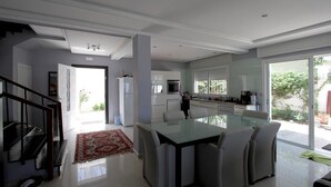 A modern kitchen with a glass dining table, white cabinets, and a view of the outdoors.