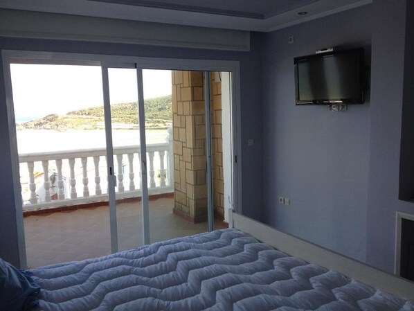 A bedroom with a bed, a TV mounted on the wall, and a balcony with a view of the beach. - Villa Tanger Cap Spartel (Tangier)
