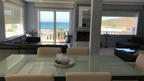 A modern living room with a glass dining table, beige sofas, and a view of the ocean through large windows.