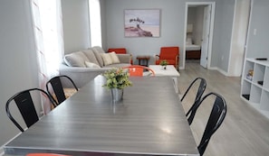A dining area with a table, chairs, and a vase with greenery. There is a sofa and a painting on the wall in the background. - 1 Block to the Beach~3BR Condo~ Budget Friendly (Gulf Shores)