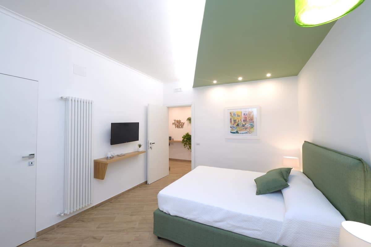 Ein modernes Schlafzimmer mit einem grünen Kopfteil, einem flachbildfernseher an der Wand, einem Nachttisch und einem grünen Kissen.