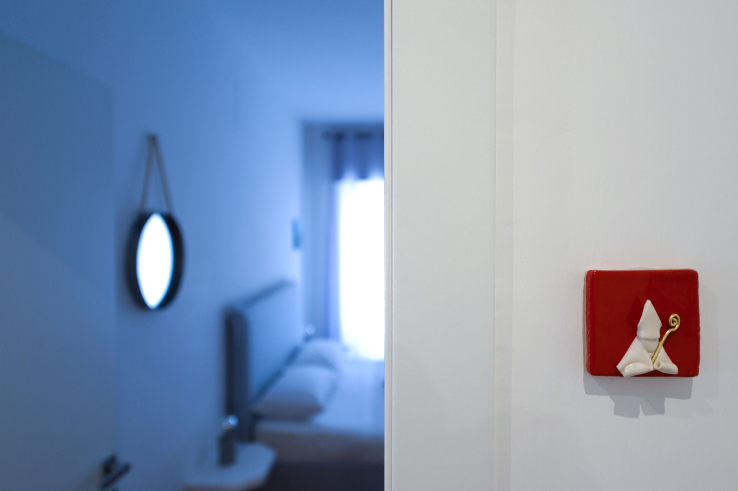 A room with a blue wall, a round mirror, and a red object on the wall.
