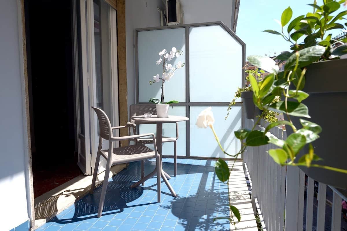 Ein kleiner Balkon mit Tisch und zwei Stühlen, einem Blumentopf und einer weißen Rose.