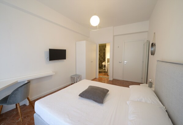 A modern hotel room with a large bed, a flat-screen TV mounted on the wall, a small desk, and a chair. - Il SanFilippo Apartments and Rooms (Naples)