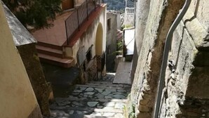 A narrow stone pathway leading to a building with a metal railing and a street lamp. - A Taverna Intru u vicu (Belmonte Calabro)