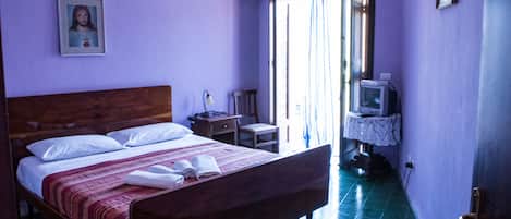 A bedroom with a wooden bed, a small bedside table, a chair, a television, and a window with curtains.