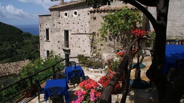 A rustic stone building with a terrace, outdoor seating, and a view of the sea. - A Taverna Intru u vicu (Belmonte Calabro)