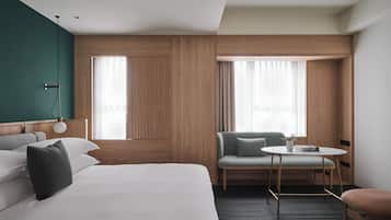A hotel room with a bed, a chair, a small table, and a window.