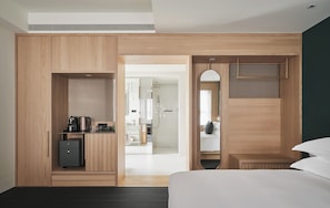 Een moderne hotelkamer met een houten kledingkast, een klein bureau met een waterkoker, een bed en een spiegel.