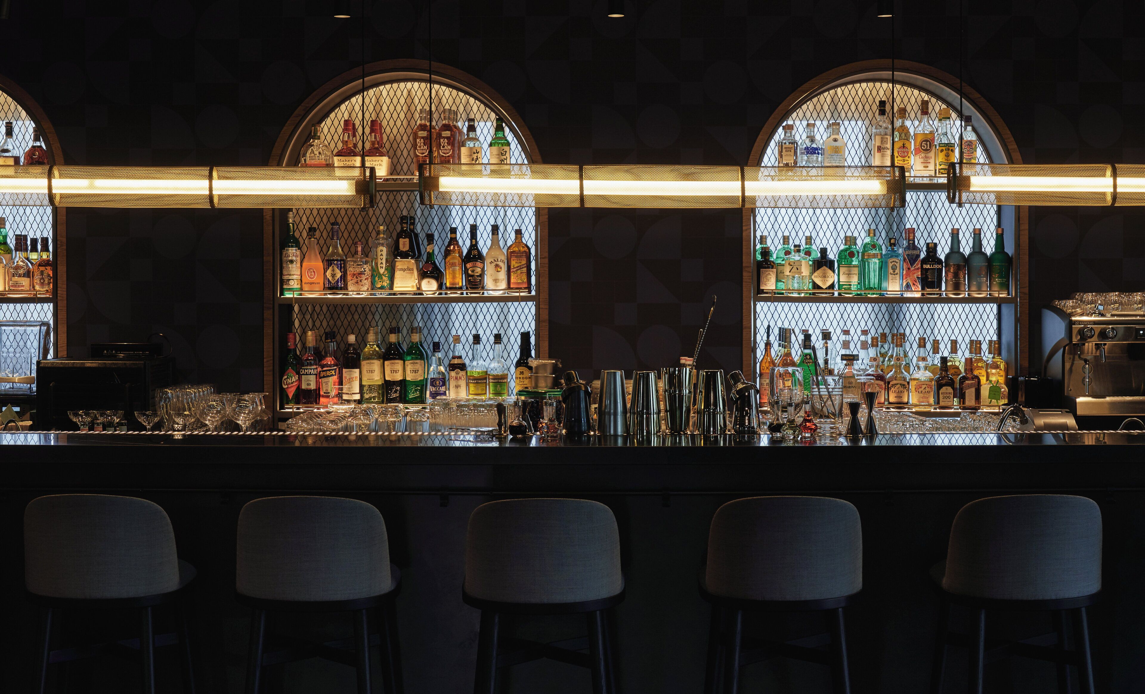 A bar with multiple shelves of liquor bottles, a coffee machine, and bar stools.