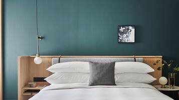 Una cama bien tendida con ropa blanca, un cabecero de madera y una mesita de noche con una lámpara y un pequeño florero.