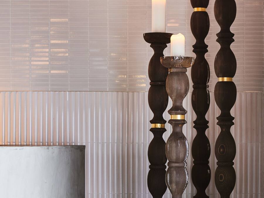 Tres portavelas con velas, un banco de metal y una pared de azulejos.