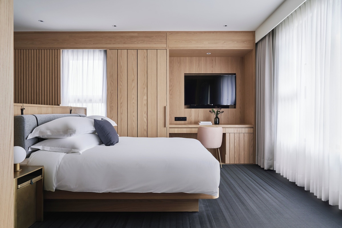 Une chambre d’hôtel moderne dotée d’un grand lit, d’un bureau, d’une télévision à écran plat et d’une fenêtre avec des rideaux.