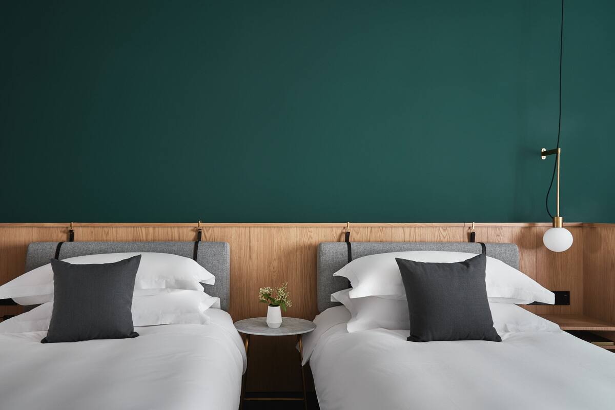 Une chambre d’hôtel avec deux lits, une table ronde ornée d’un vase de fleurs et une lampe fixée au mur.