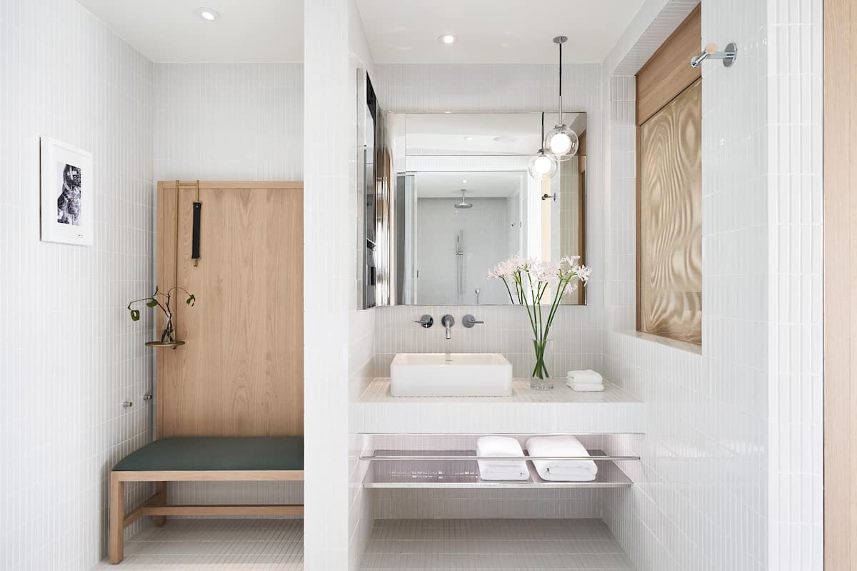 Une salle de bain moderne avec un banc en bois, un grand miroir, un lavabo et un espace douche.