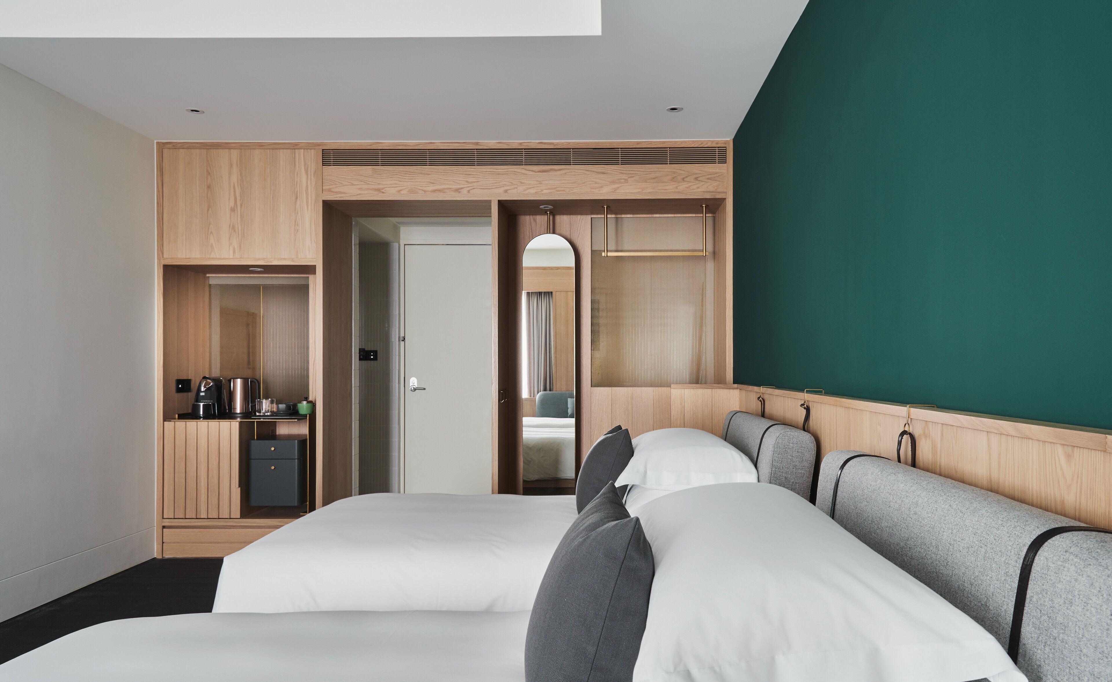Ein modernes Hotelzimmer mit zwei Betten, einer Küchenzeile, einem Kleiderschrank und einer Wand in Grünton.